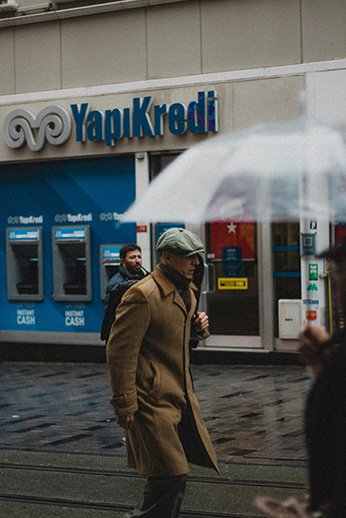 a man walking in the rain across an ATM Machines on a busy street.